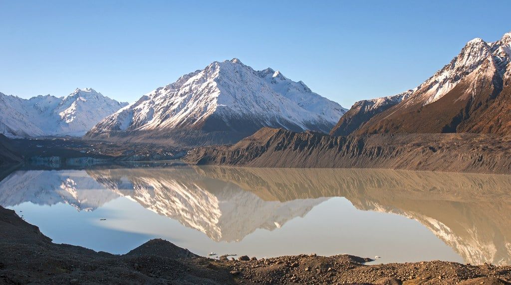 Snow-covered peaks reflect across the still waters of Tasman Glacier Lake at Aoraki/Mount Cook National Park in winter.