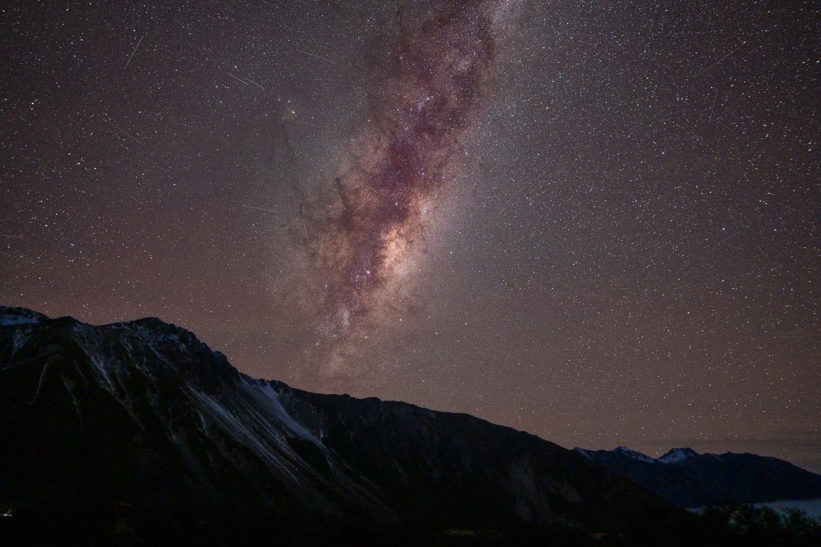 Milky Way galaxy arches across the starry night sky over the mountain ridges near Mount Cook.