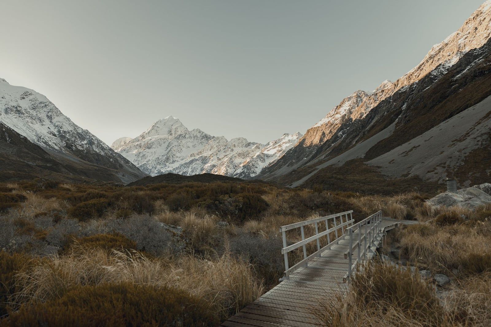 A frost-covered wooden footbridge on the Hooker Valley Track leading toward snow-capped Mount Cook.