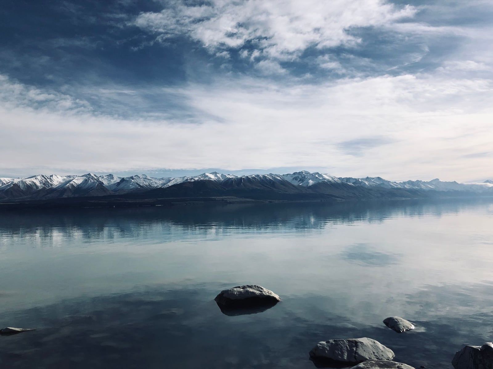 Snow-covered peaks of the Southern Alps reflect across the calm waters of Lake Pukaki in winter.